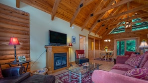 A cozy cabin interior with a fireplace, wooden walls, a television, and a plush red sofa. - Spacious Log Cabin in community with Lake and River Access. (Lake Lure)