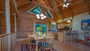 A wooden cabin interior with a dining area, kitchen, and large windows. - Spacious Log Cabin in community with Lake and River Access. (Lake Lure)