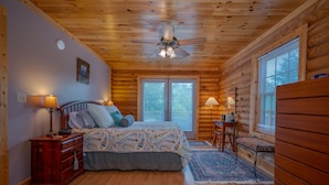 A log cabin bedroom with a bed, nightstands, a wooden dresser, and a ceiling fan. - Spacious Log Cabin in community with Lake and River Access. (Lake Lure)