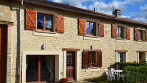 Un bâtiment en pierre avec des volets en bois, une porte-fenêtre coulissante et un petit espace extérieur aménagé avec une table et des chaises.