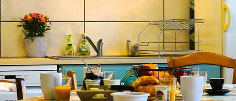 A breakfast table with various food items, a vase with flowers, and kitchen appliances.