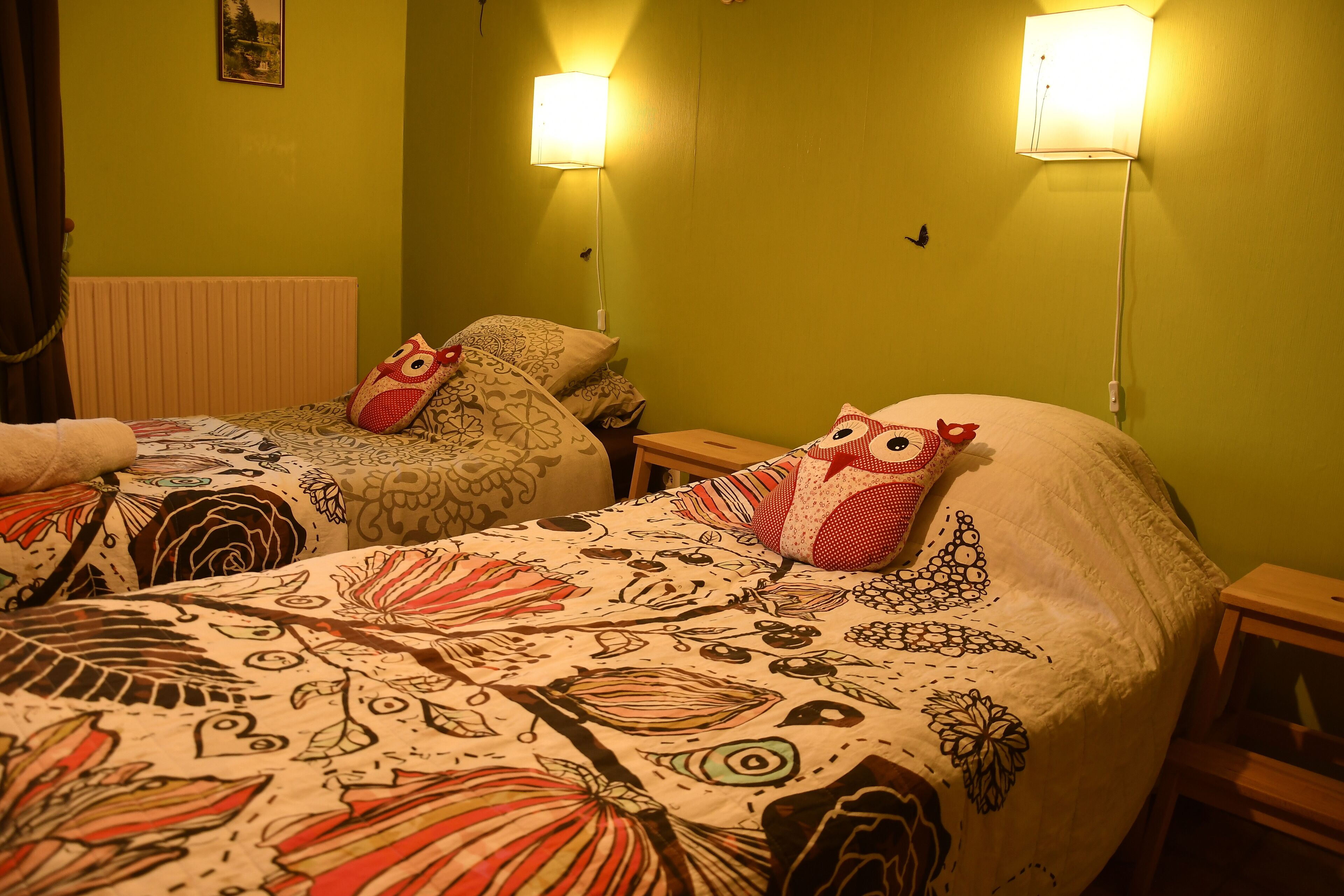 A room with two beds, each with patterned bedding and matching pillows. There are wall-mounted lamps on either side of the beds.