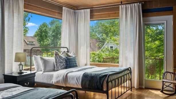A bedroom with a large window, a bed, a bedside table, and a chair.