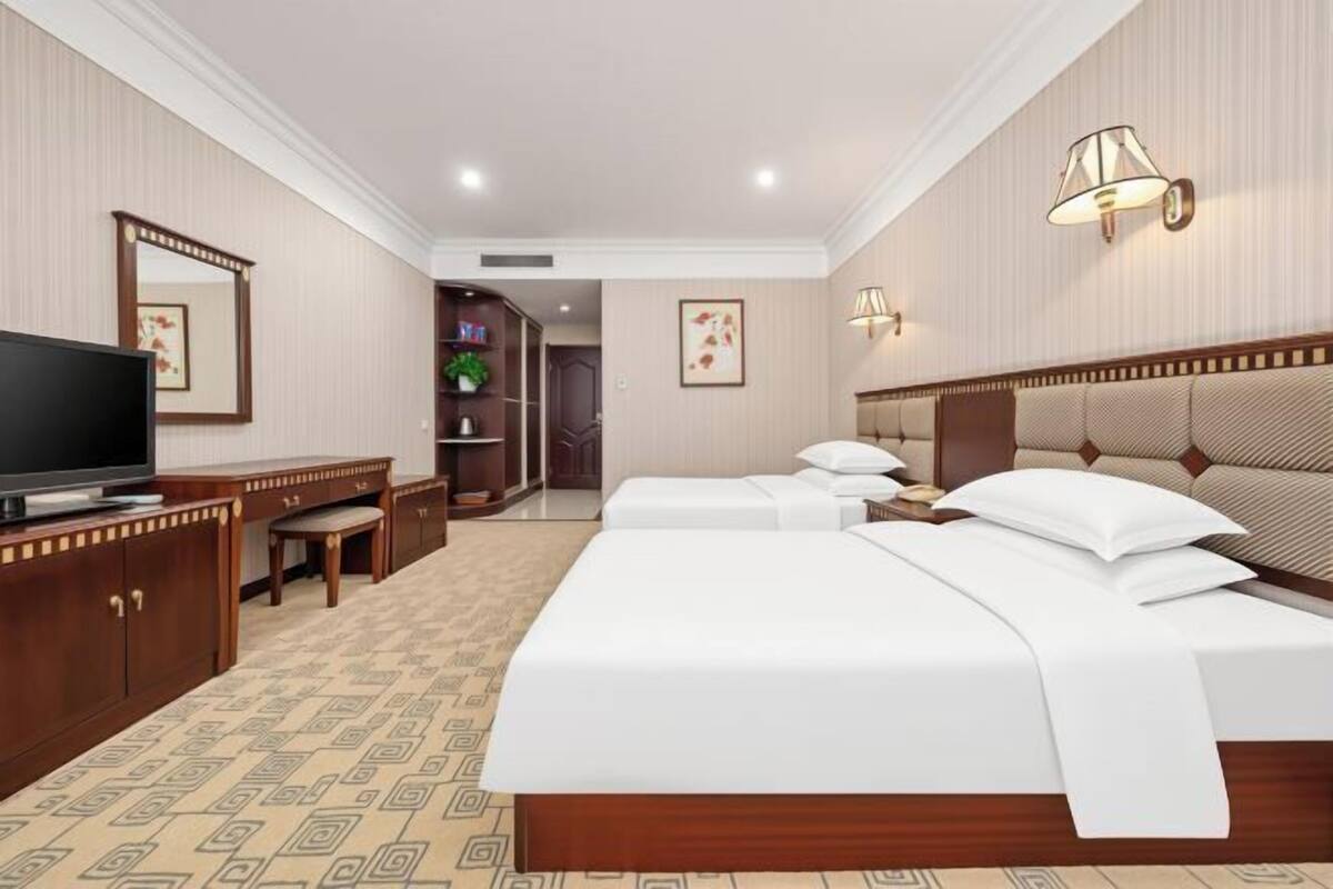 Une chambre d’hôtel avec un grand lit, un bureau avec une télévision, un miroir et deux lampes fixées au mur.