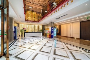 Um saguão de hotel com balcão de recepção, um espelho grande e piso estampado.
