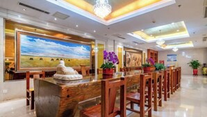 A reception area with a long wooden reception desk, chairs, a large painting, and potted plants.
