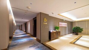 A hotel corridor with a reception desk, a plant, and a painting on the wall.