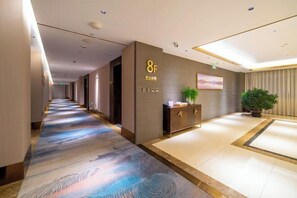 A hotel corridor with a reception desk, a plant, and a painting on the wall. - Niu De Cao Hotel (Shenzhou)
