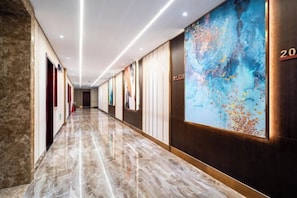 Un pasillo de hotel con piso de mármol, paneles de madera y un cuadro abstracto grande en la pared derecha.