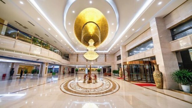 A spacious lobby with a central chandelier, multiple levels, and a red carpet leading to the entrance.