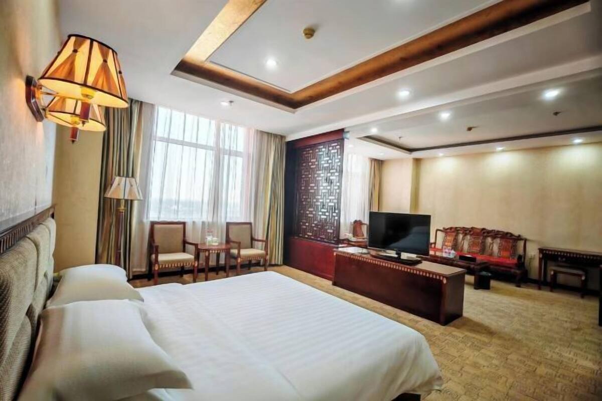 Une chambre d’hôtel avec un grand lit, un bureau avec une télévision, un coin salon avec des fauteuils et un mur décoratif.