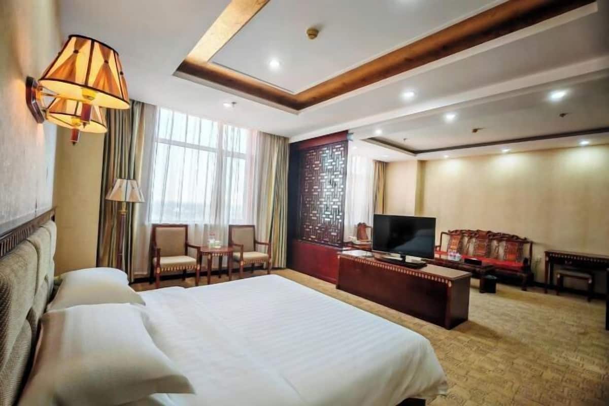 A hotel room with a large bed, a desk with a TV, a seating area with chairs, and a decorative wall.