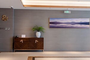 Un moderno vestíbulo de hotel con un cuadro grande de montañas, un mueble de madera con una planta y un cartel que indica una salida.