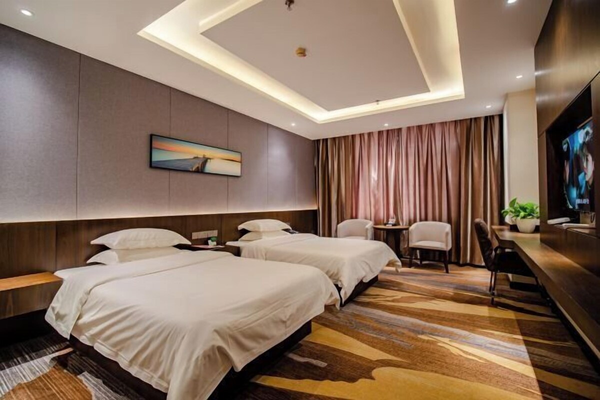 Ein Hotelzimmer mit zwei Betten, einem Schreibtisch, einem Sessel, einem Fernseher und einem Bild an der Wand.
