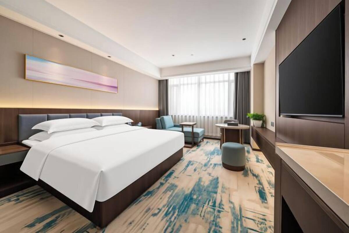 Une chambre d’hôtel moderne équipée d’un grand lit, d’un bureau, d’une chaise, d’une télévision et d’une fenêtre avec des rideaux.