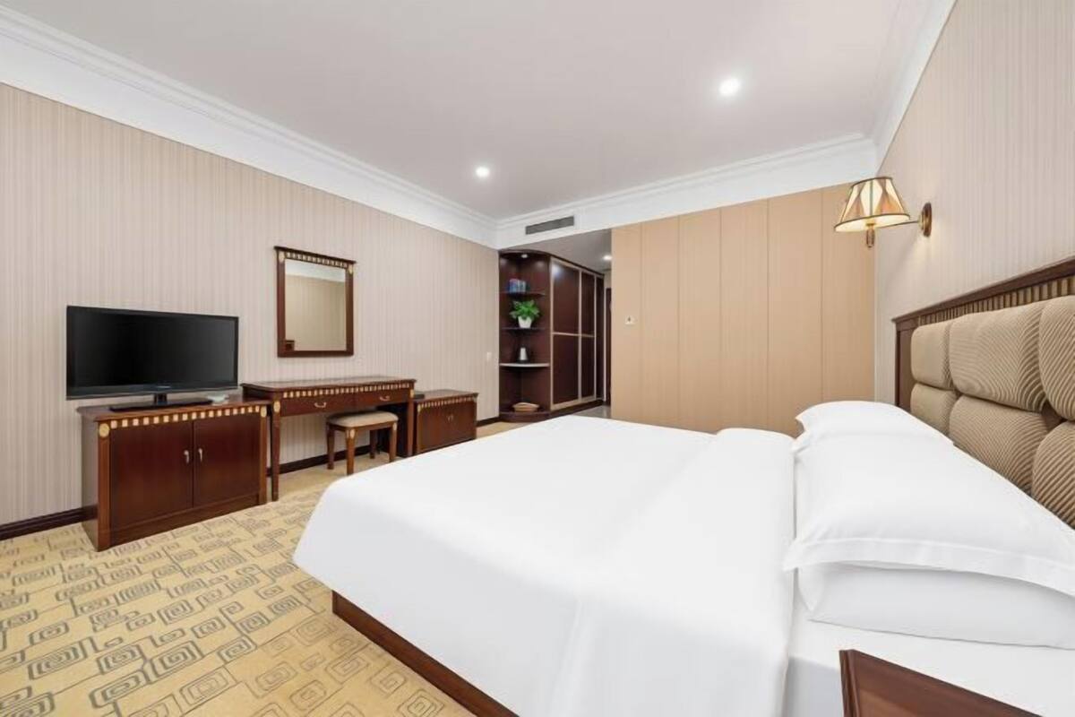 Une chambre d’hôtel comprenant un lit, un bureau avec une chaise, une télévision, un miroir, une armoire et une lampe.
