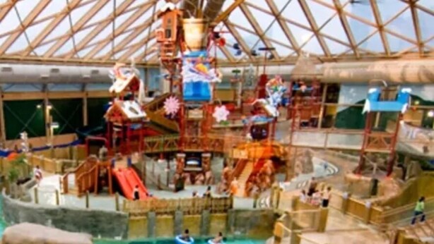 Parque acuático interior con múltiples toboganes, una piscina grande y balsas inflables.