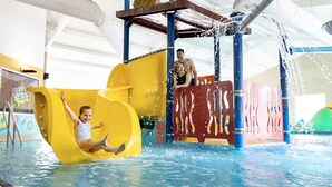 Uma criança escorrega em um escorregador aquático amarelo em uma área de piscina, com um homem parado perto.