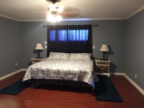 A bedroom with a bed, two bedside tables with lamps, a ceiling fan, and a dark blue curtain.