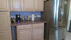 A kitchen with light wood cabinets, a stainless steel refrigerator, a coffee maker, and three mugs with messages. - Orange Blossom Refuge (Pinellas County)