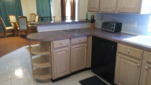 A kitchen with a dishwasher, a toaster, and a dining area with chairs and a table. - Orange Blossom Refuge (Pinellas County)