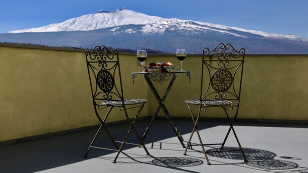 A balcony with two metal chairs and a small table, set against a yellow wall with a view of a snow-capped mountain. - Charming Bed and Breakfast in Castiglione di Sicilia (Castiglione di Sicilia)
