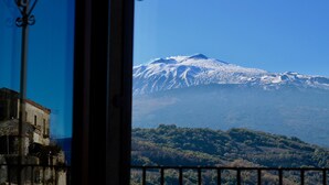 A mountain with snow-capped peaks, a view of a forested area, and a building with a balcony. - Charming Bed and Breakfast in Castiglione di Sicilia (Castiglione di Sicilia)