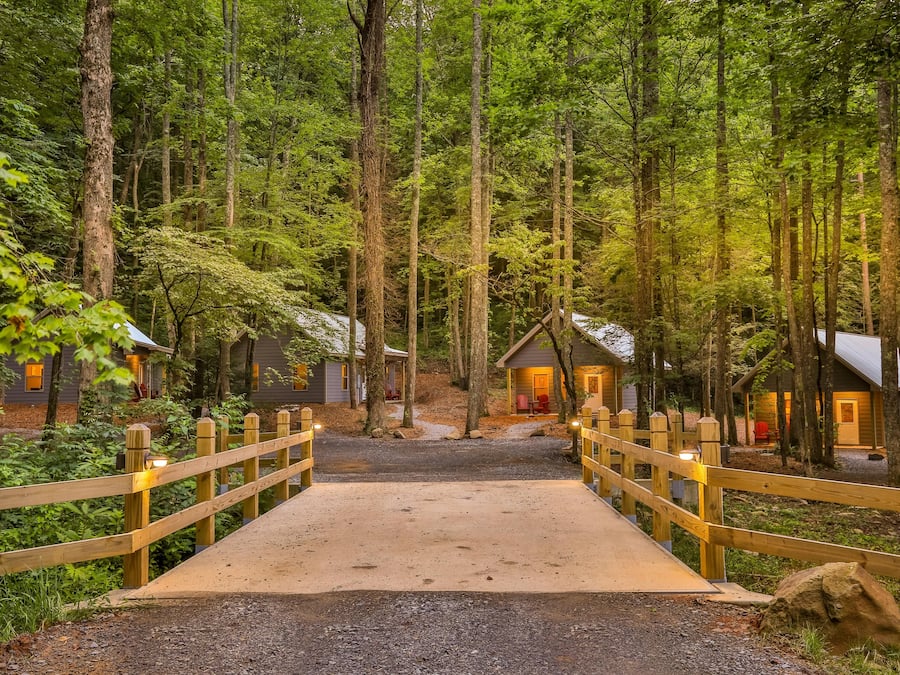 A wooden bridge leading to a row of cabins in a forested area.
