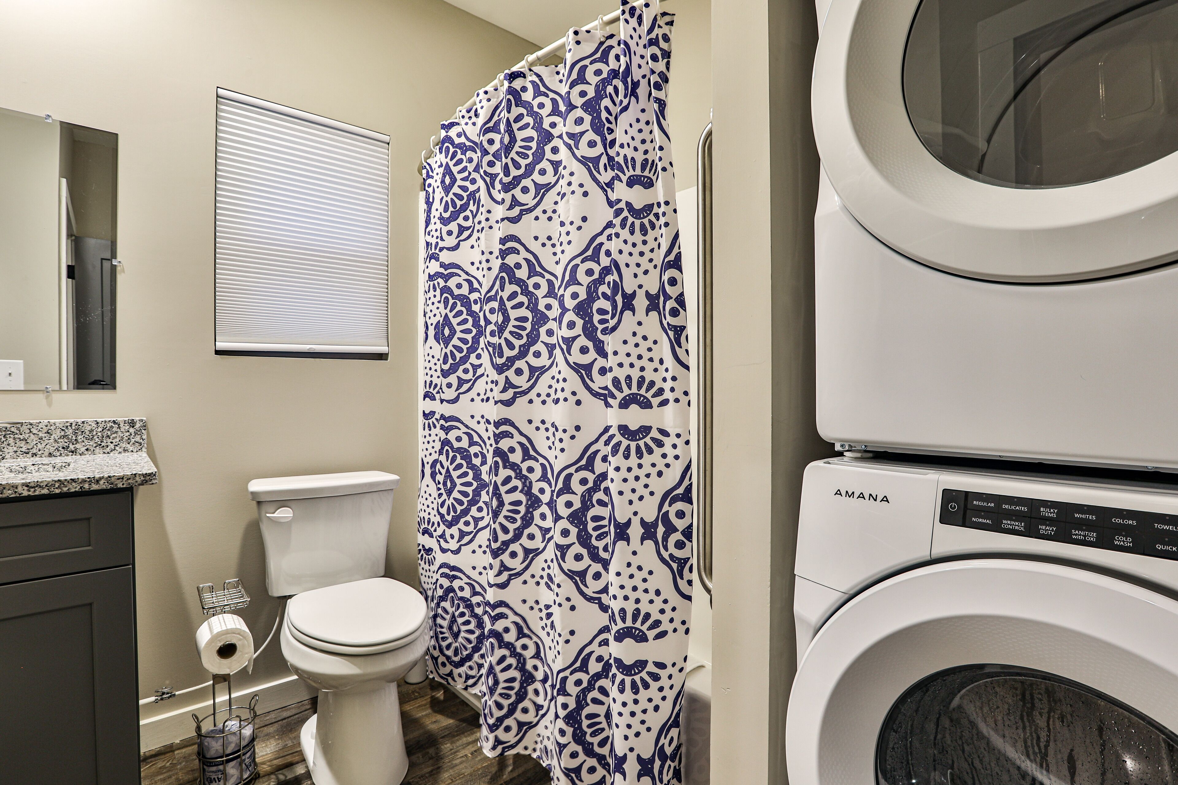 A bathroom with a toilet, a patterned shower curtain, and a stacked washer and dryer.