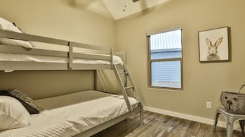Habitación con literas, una escalera, una ventana con persianas, un cuadro en la pared y una cesta de mimbre sobre un taburete.