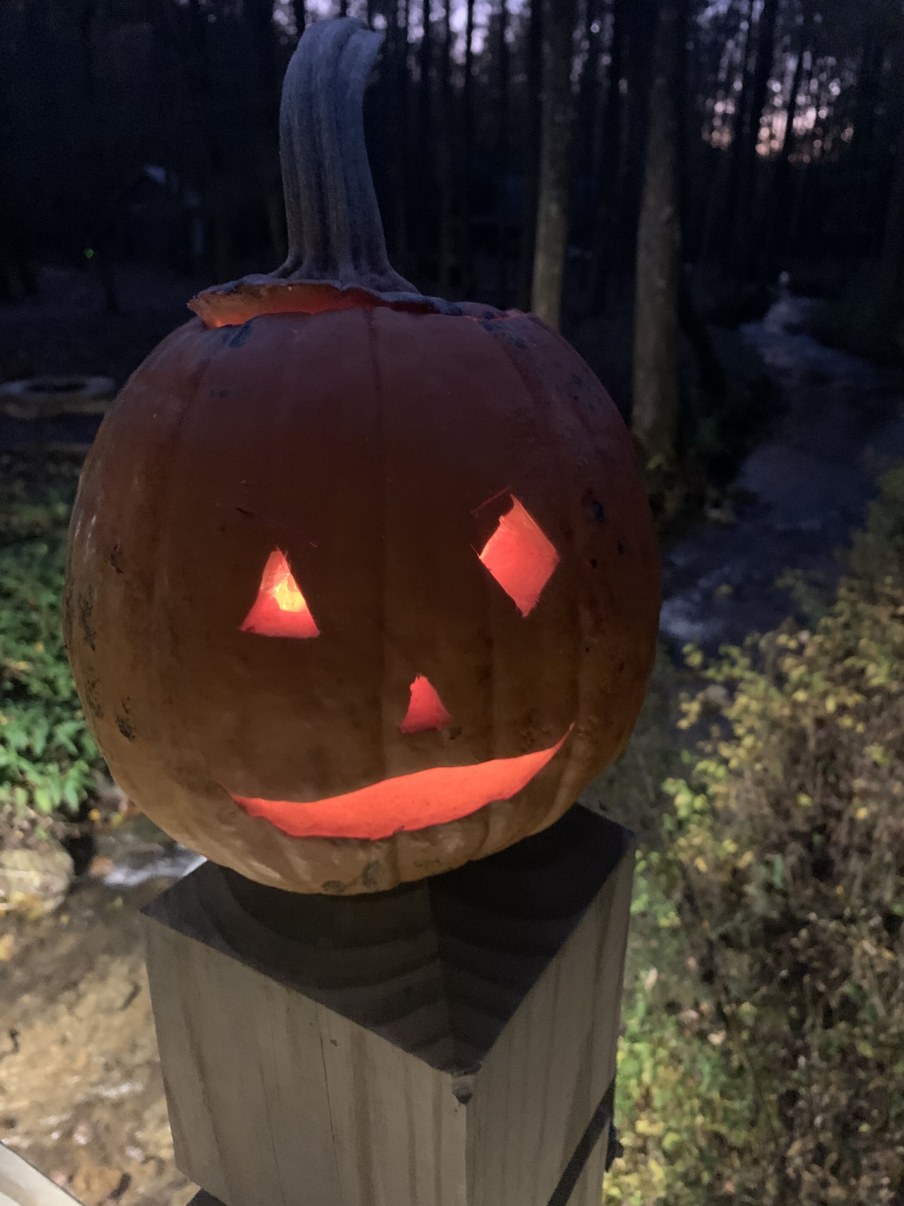 A carved pumpkin with a carved face, placed on a wooden post.