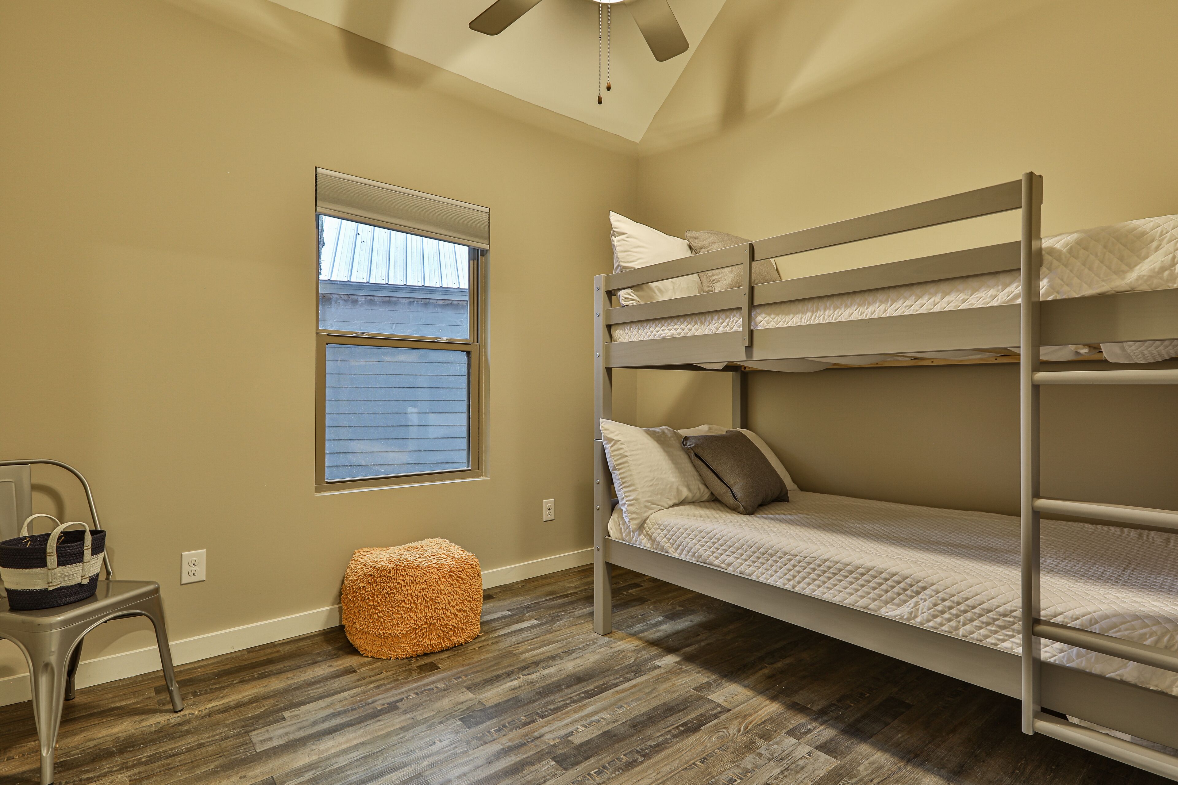 A bunk bed room with a window, a chair, and a basket.