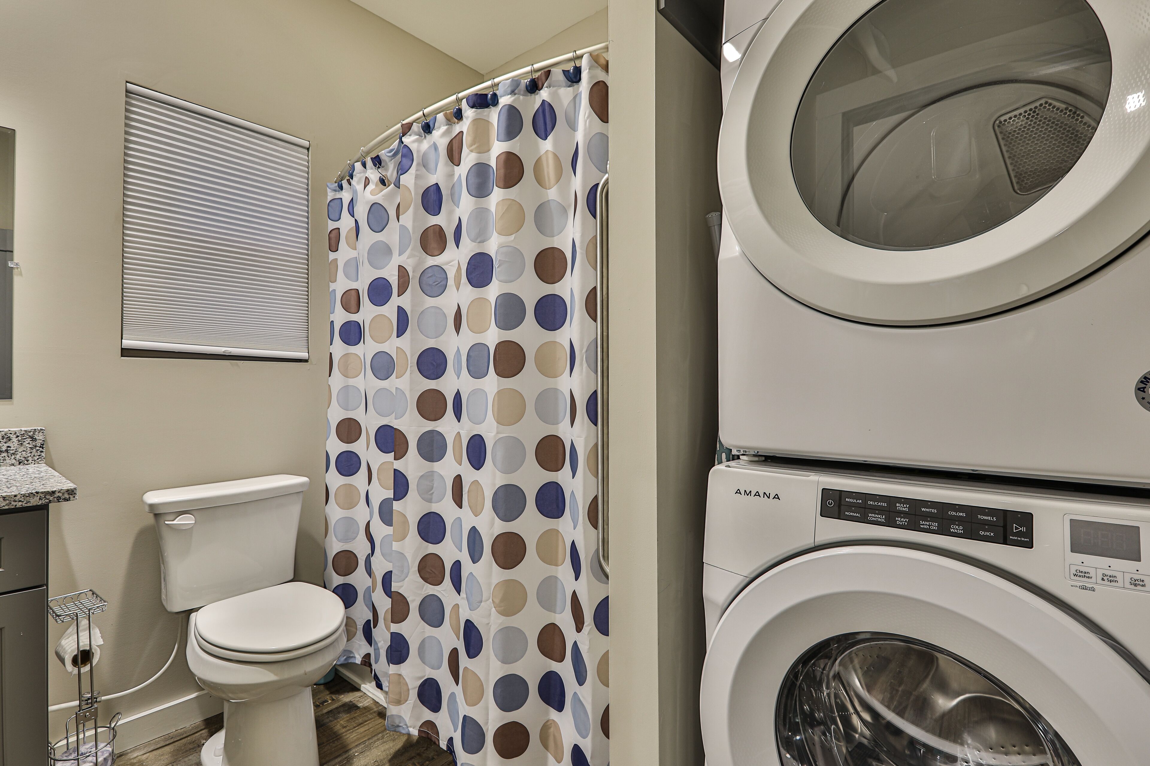 A bathroom with a toilet, a shower curtain with a polka dot pattern, and a stacked washer and dryer.