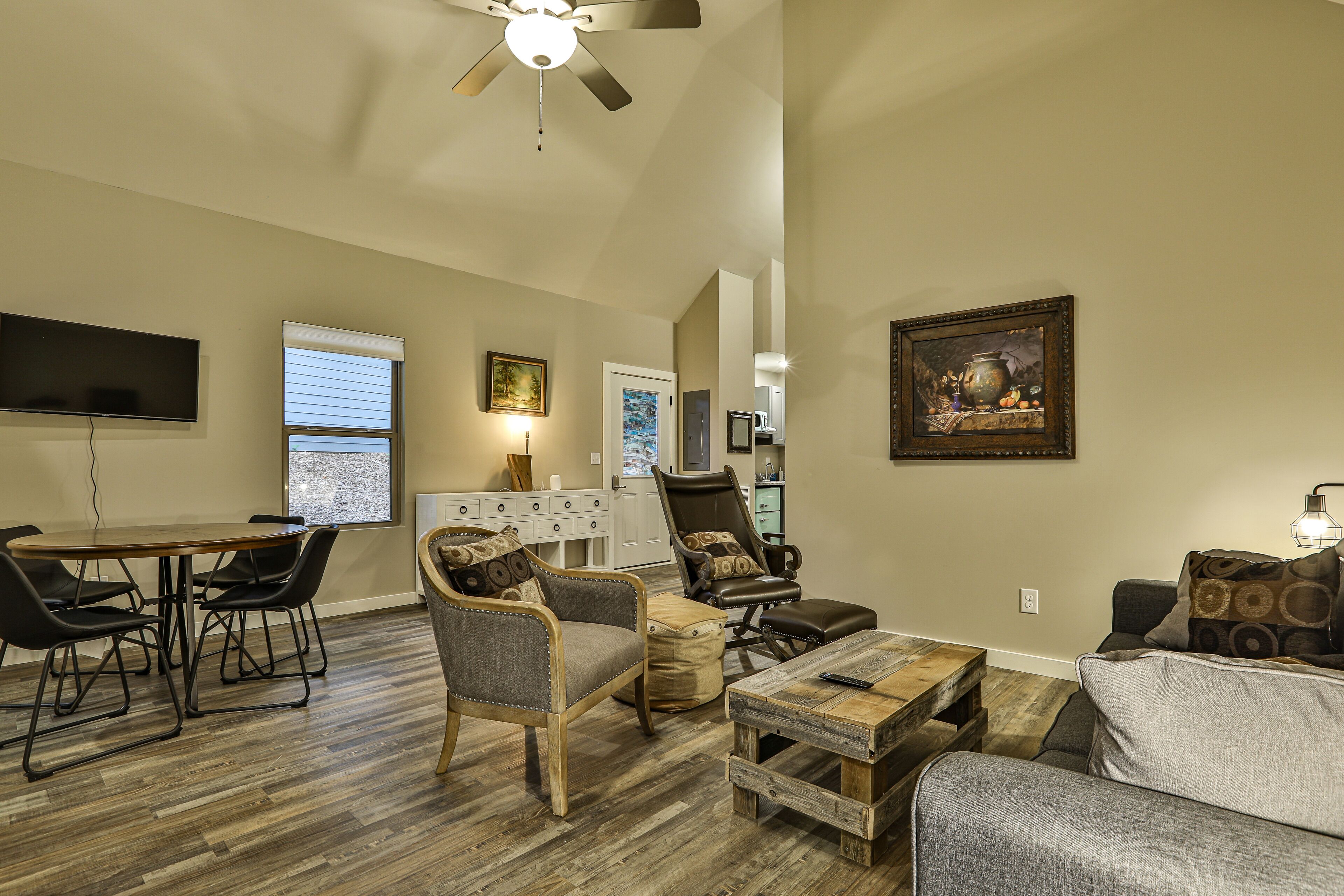 A spacious living room with a dining area, a ceiling fan, a flat-screen TV, and a painting on the wall.