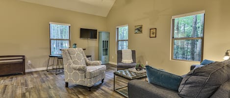 Amplia sala de estar con ventilador de techo alto, ventanas grandes y una zona de estar acogedora con sofá y sillones.