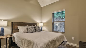 Une chambre avec un grand lit, deux lampes de chevet, une fenêtre donnant sur des arbres et un ventilateur de plafond.