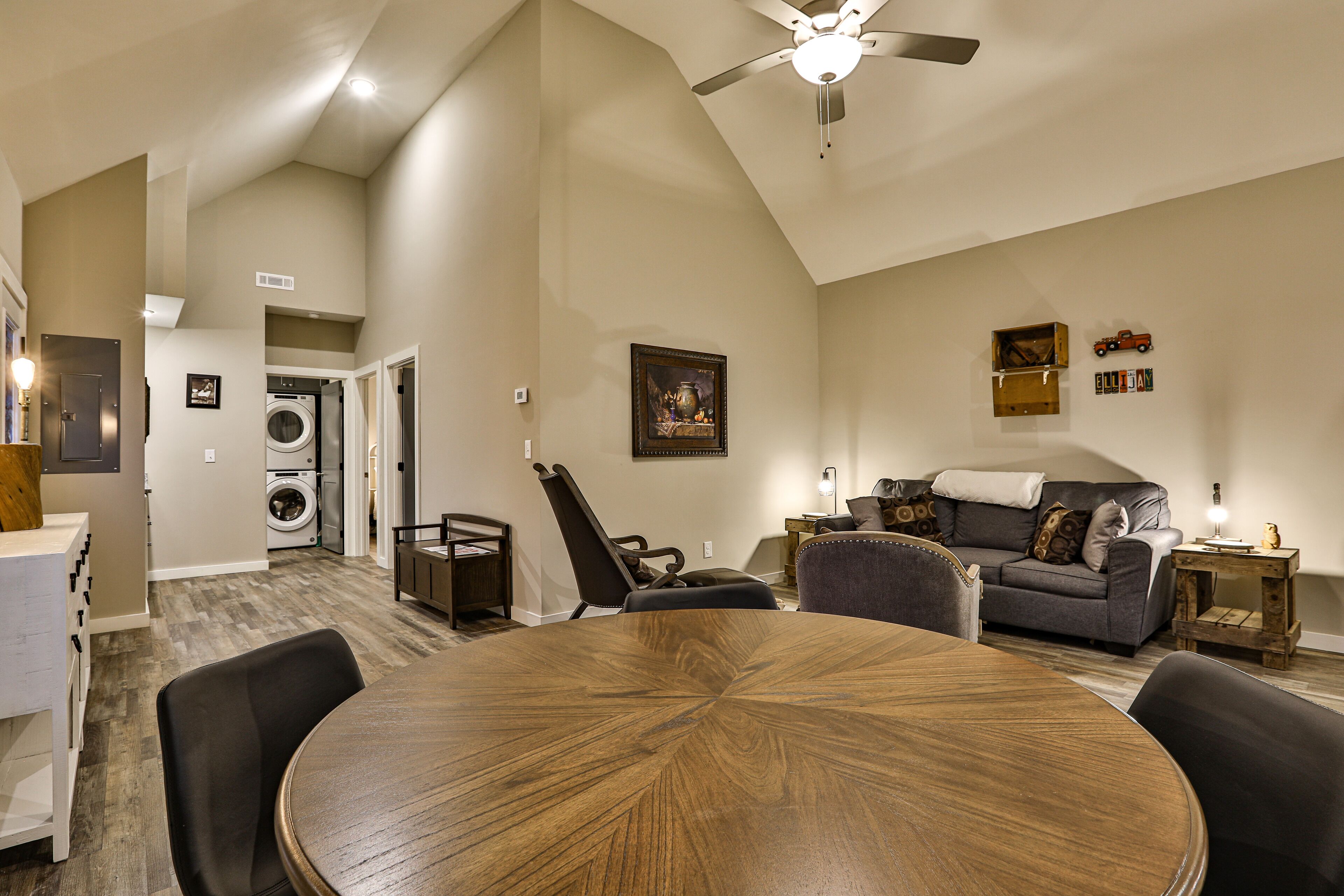 A spacious living area with a round wooden table, a gray sofa, and a ceiling fan.