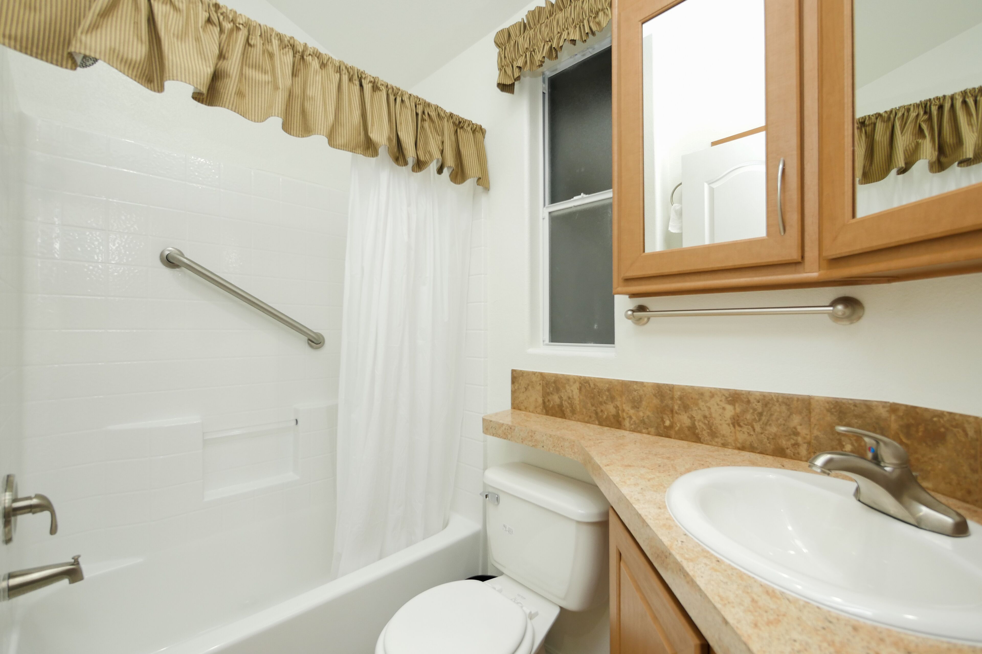A bathroom with a bathtub, toilet, sink, and a mirror above the sink.