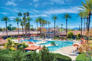 A resort with multiple swimming pools, palm trees, and a mountainous backdrop. - The Cottages at Golden Village Palms RV Resort (Hemet)