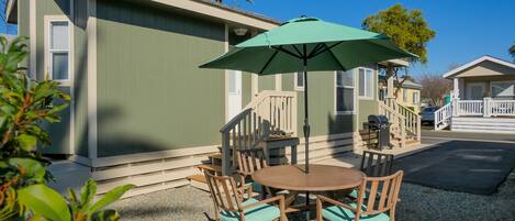 A patio with a round wooden table and chairs, an umbrella, and a staircase leading to a deck.