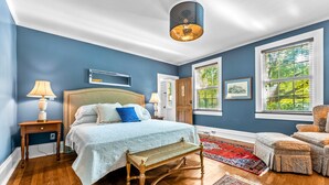 Ein Schlafzimmer mit einem großen Bett, Holzboden und Blick auf Grün durch das Fenster.