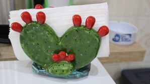 Una escultura de cactus con espinas rojas y cuerpo verde, sobre una superficie blanca.
