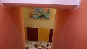 Un pasillo con un cuadro de cactus en la pared, suelo de baldosas y una puerta con marco rosa.