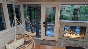 A cozy room with a hanging chair, a fireplace, and a view of a forest through large windows. - Ultra Private, Crooked Reflections, Riverside Retreat, Hot Tub, Waterfront Glass (Norway)