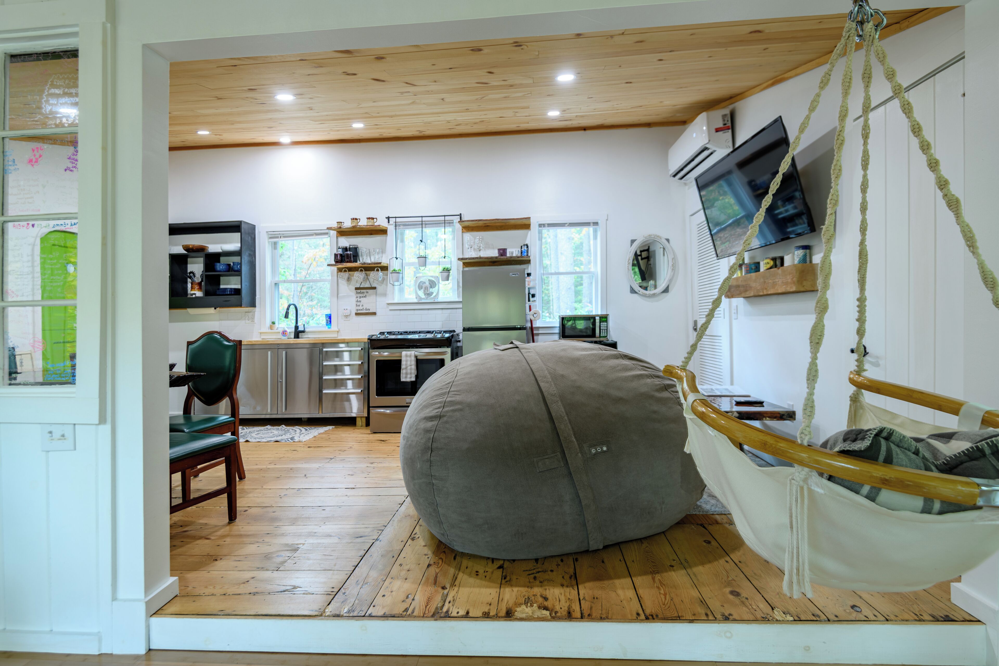 Une pièce spacieuse avec un grand fauteuil en forme de poire, un plancher en bois, un coin cuisine équipé d’appareils électroménagers modernes et une balançoire suspendue.