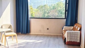 Una habitación con un ventanal grande, suelo de madera, una silla blanca y un sofá con una manta estampada.