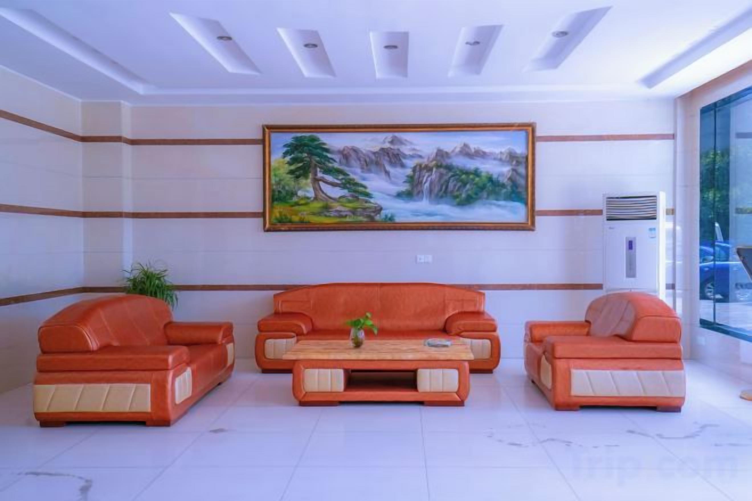 A lobby with three orange sofas, a wooden coffee table, and a painting of a landscape on the wall.
