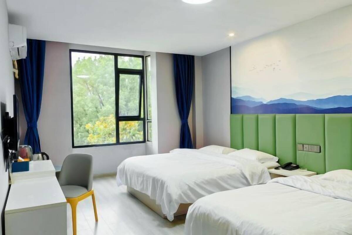 Habitación de hotel con dos camas, un escritorio, una silla y un ventanal con vistas a zonas verdes.