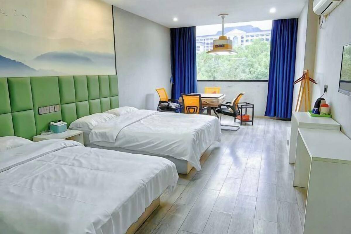 Habitación de hotel con dos camas, un escritorio, sillas, una mesa y una ventana con cortinas.