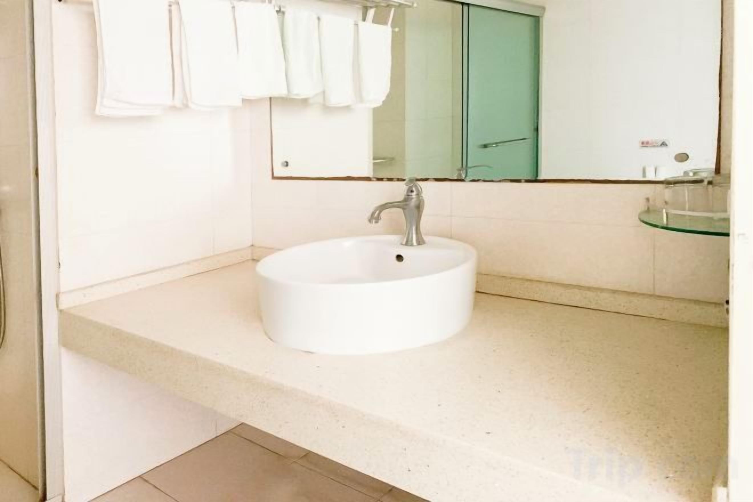 Un baño con un lavamanos blanco, un espejo y una repisa de vidrio.